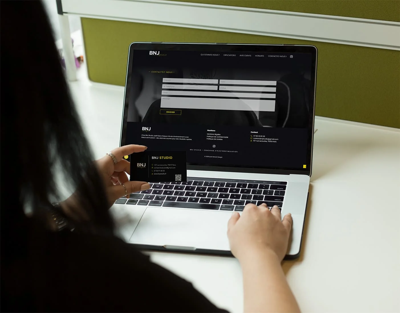 alt="Femme de dos parcourant le site web de BNJ Studio en tenant une de leur carte de visite"