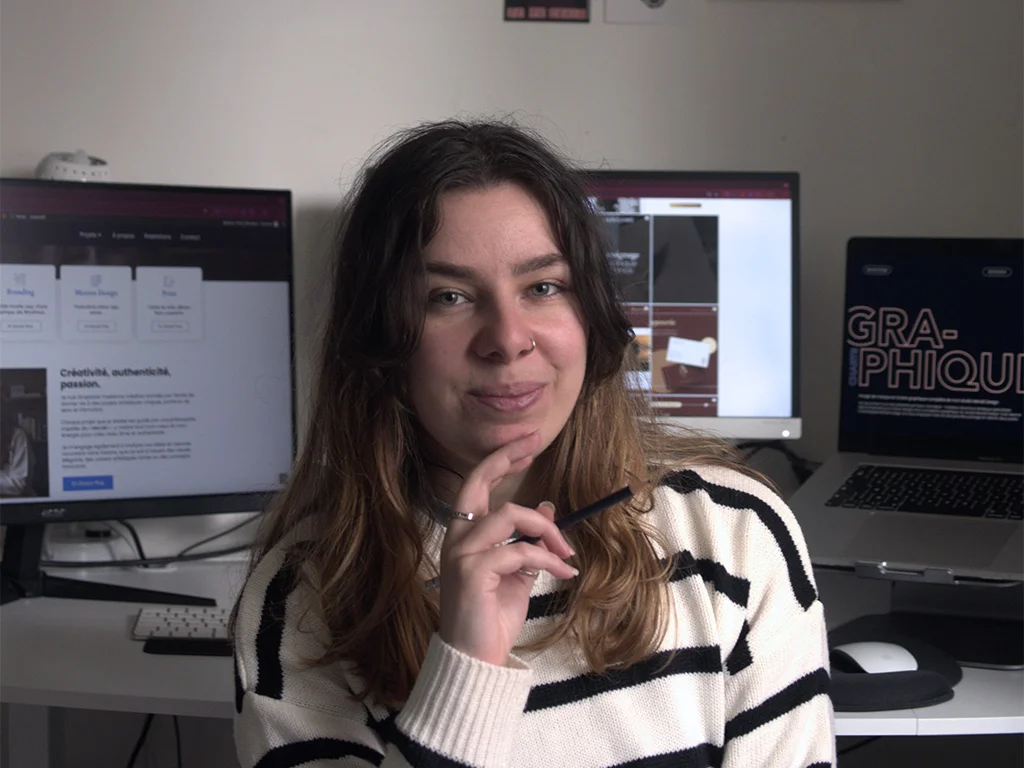 alt="Graphiste & DA souriant devant ses écrans d'ordinateur et son blog"