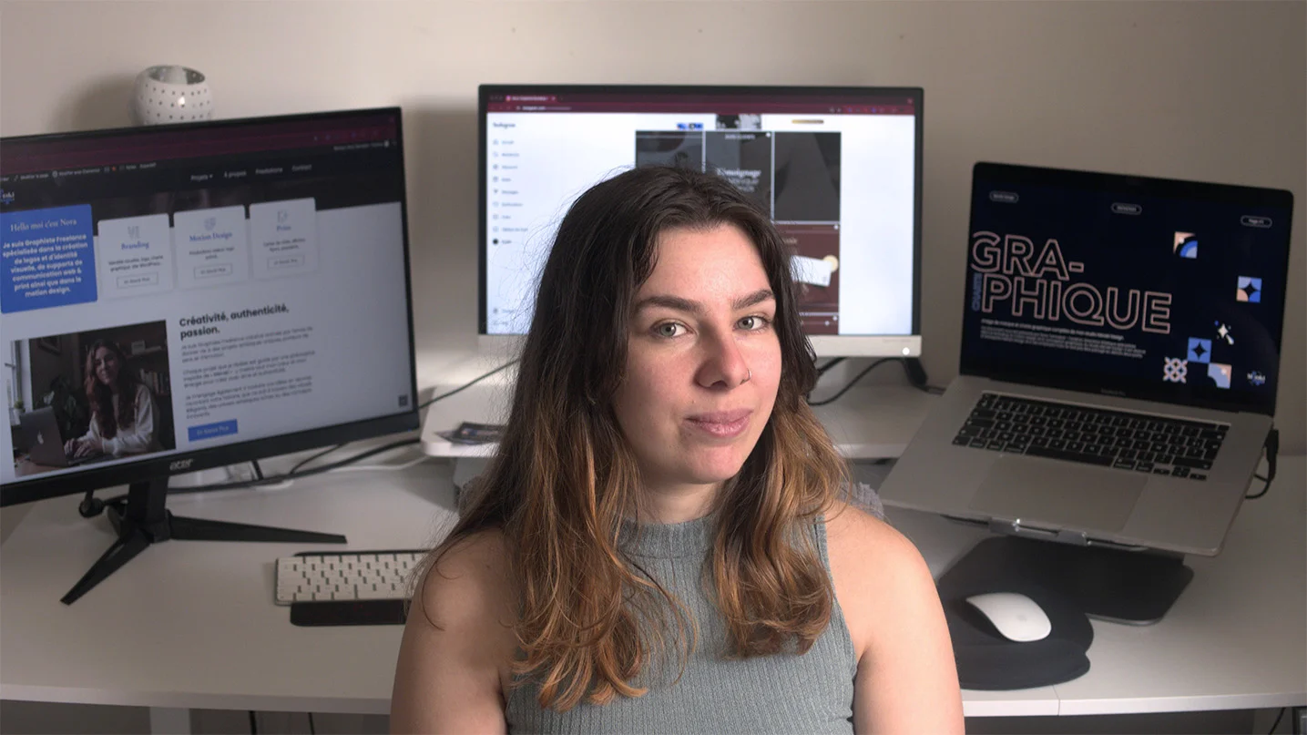alt="Nora, Graphiste & DA souriant devant ses 3 écrans d'ordinateur"